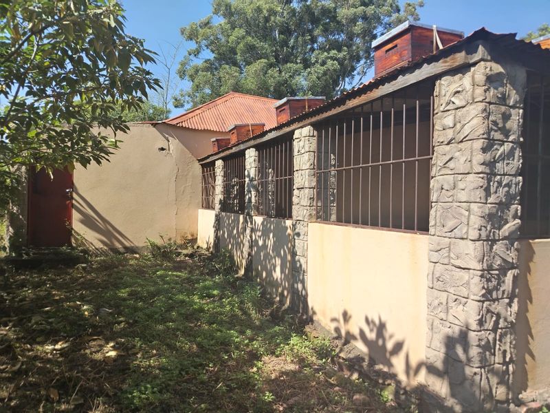 Rear exterior view of a farm building featuring stone-clad pillars, metal security bars, and corrugated roofing with integrated beehive structures.