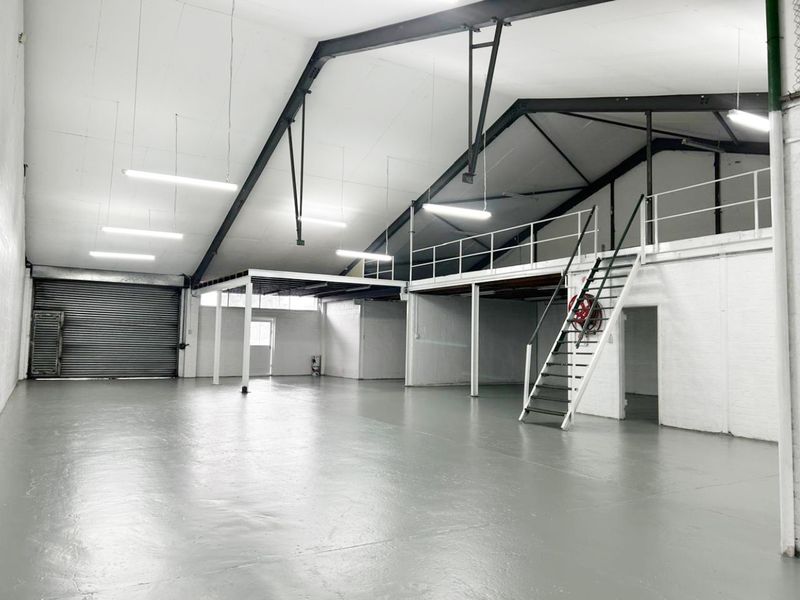 Spacious industrial warehouse unit featuring a mezzanine level, steel staircase, roller shutter door, and durable epoxy-coated flooring, suitable for various commercial or storage uses.