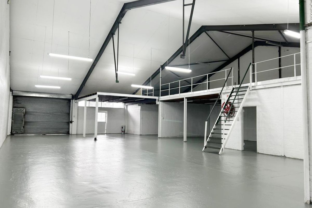 Spacious industrial warehouse unit featuring a mezzanine level, steel staircase, roller shutter door, and durable epoxy-coated flooring, suitable for various commercial or storage uses.