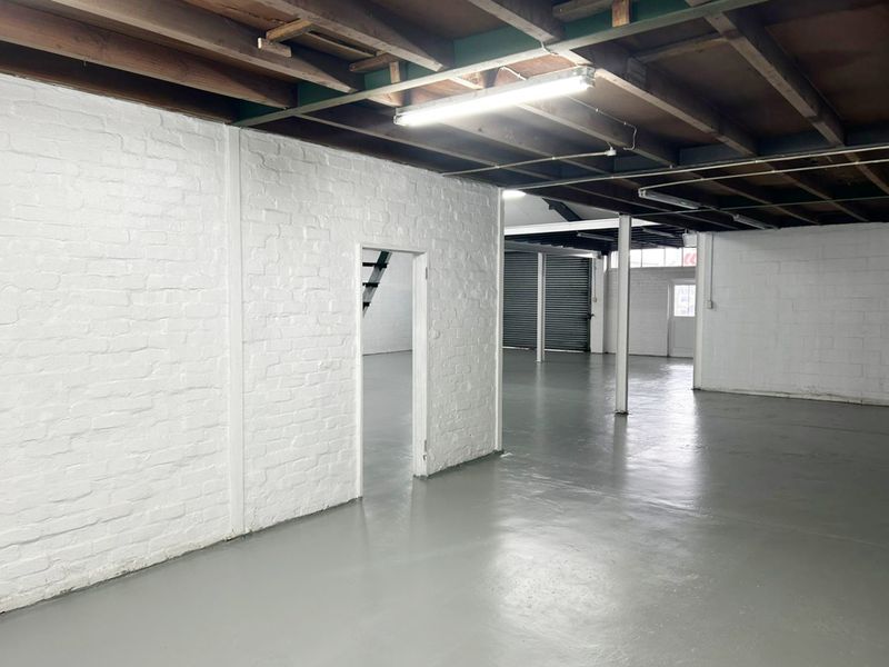 Spacious industrial utility area featuring painted brick walls, exposed timber ceiling beams, and durable epoxy-coated concrete flooring with roller shutter access.
