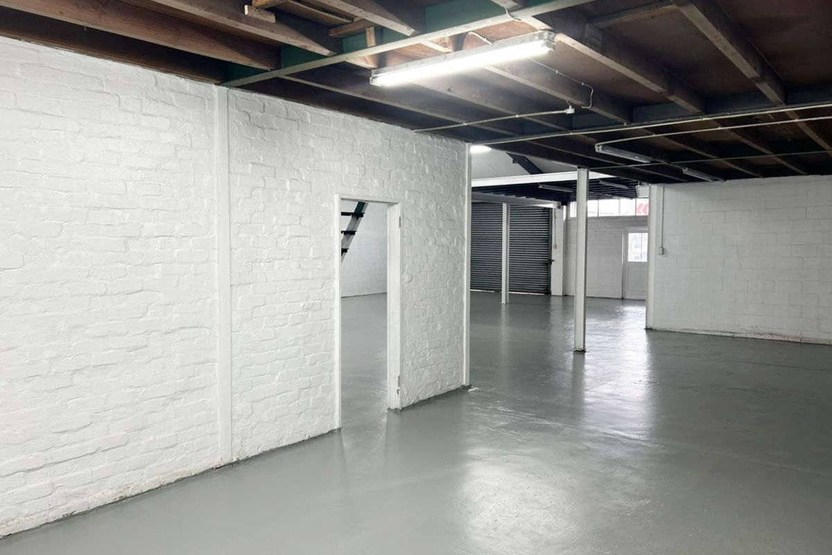 Spacious industrial utility area featuring painted brick walls, exposed timber ceiling beams, and durable epoxy-coated concrete flooring with roller shutter access.