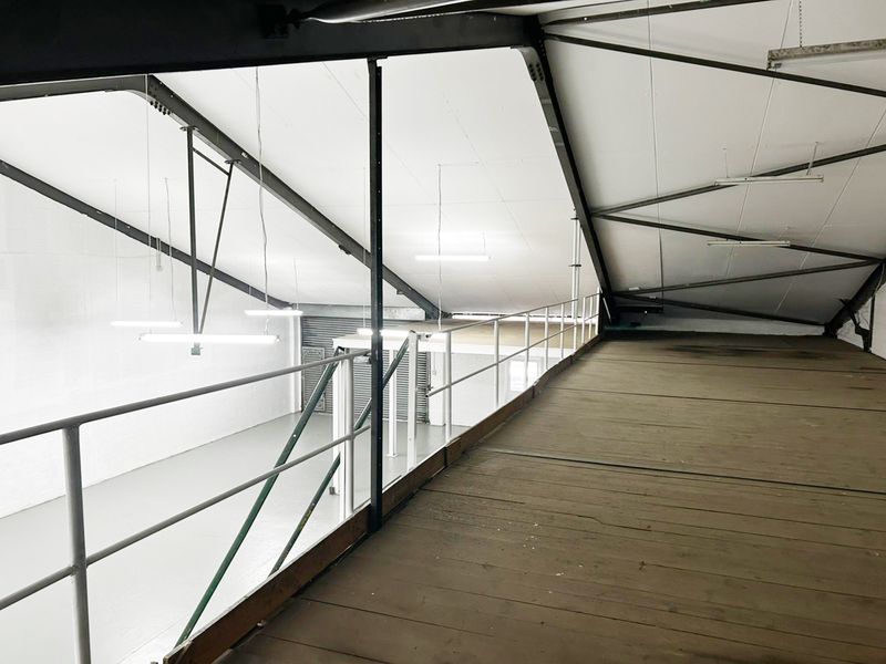 An industrial mezzanine level featuring exposed steel structural beams, timber flooring, and safety railings, overlooking the main warehouse floor area.