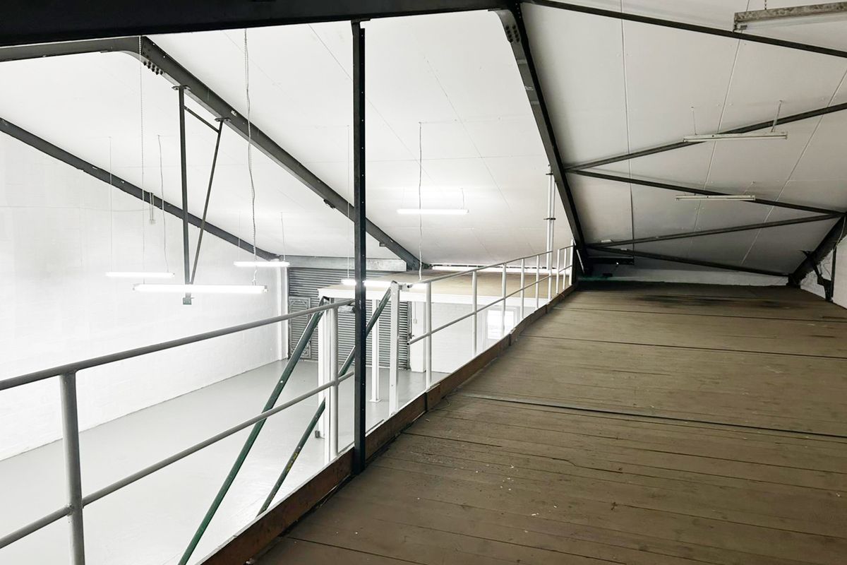 An industrial mezzanine level featuring exposed steel structural beams, timber flooring, and safety railings, overlooking the main warehouse floor area.