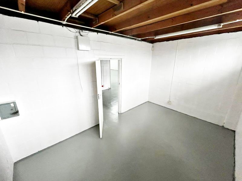 An empty utility space featuring painted concrete block walls, exposed timber ceiling joists, and a painted concrete floor with functional strip lighting.