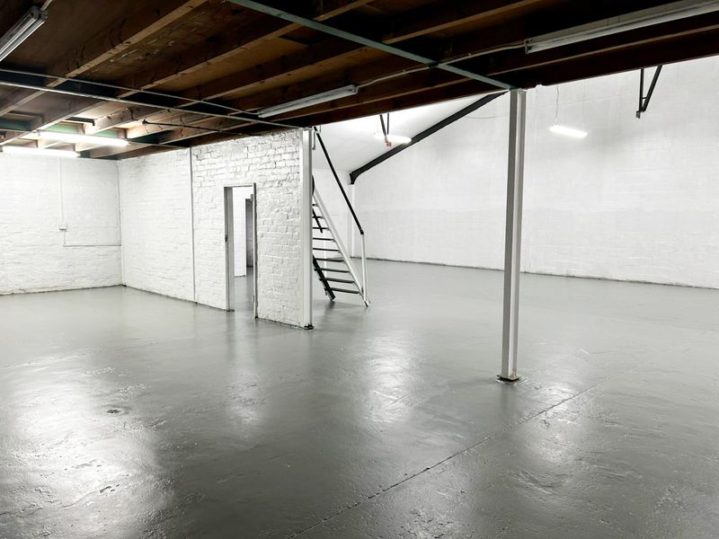Spacious industrial utility area featuring exposed timber ceiling joists, painted brick walls, durable epoxy-coated concrete flooring, and a central steel support column.