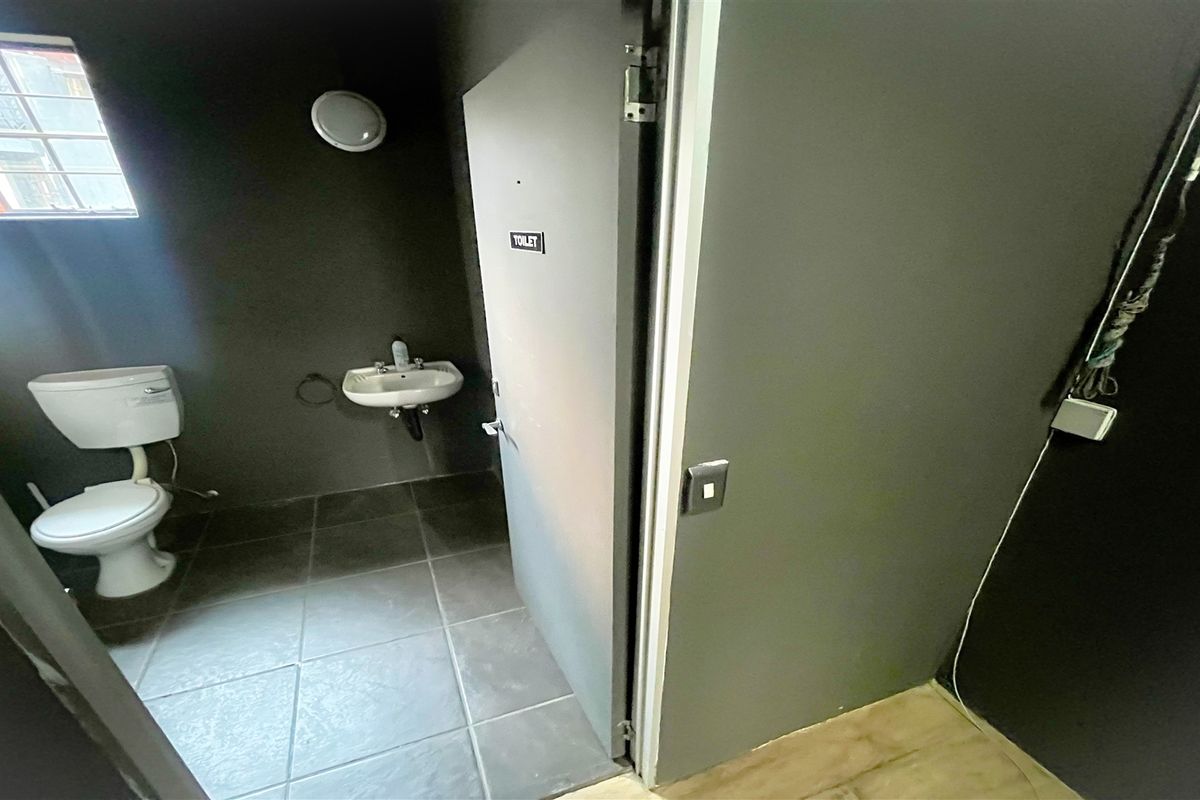 A functional office restroom featuring tiled flooring, a wall-mounted basin, and a standard toilet suite with dark-painted walls.