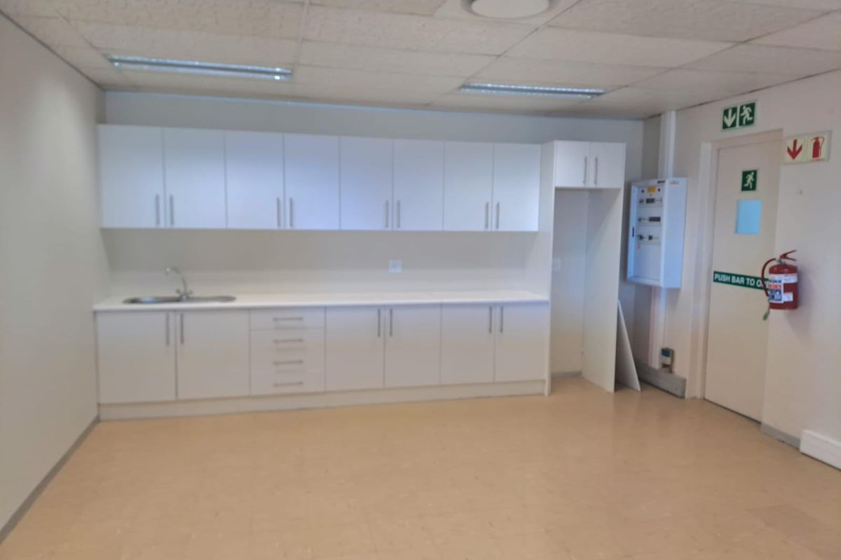 A functional office kitchenette featuring white cabinetry, a stainless steel sink, and integrated electrical distribution board.