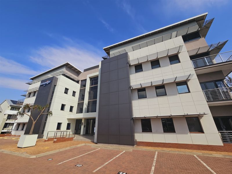 Modern multi-story office building featuring contemporary facade cladding, large glass windows, and paved parking area.