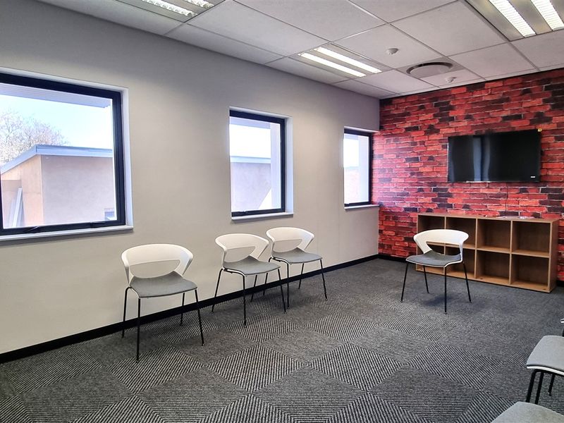 A modern office space featuring carpet tiles, a brick-effect feature wall, and recessed lighting, providing a professional environment for meetings or collaborative work.