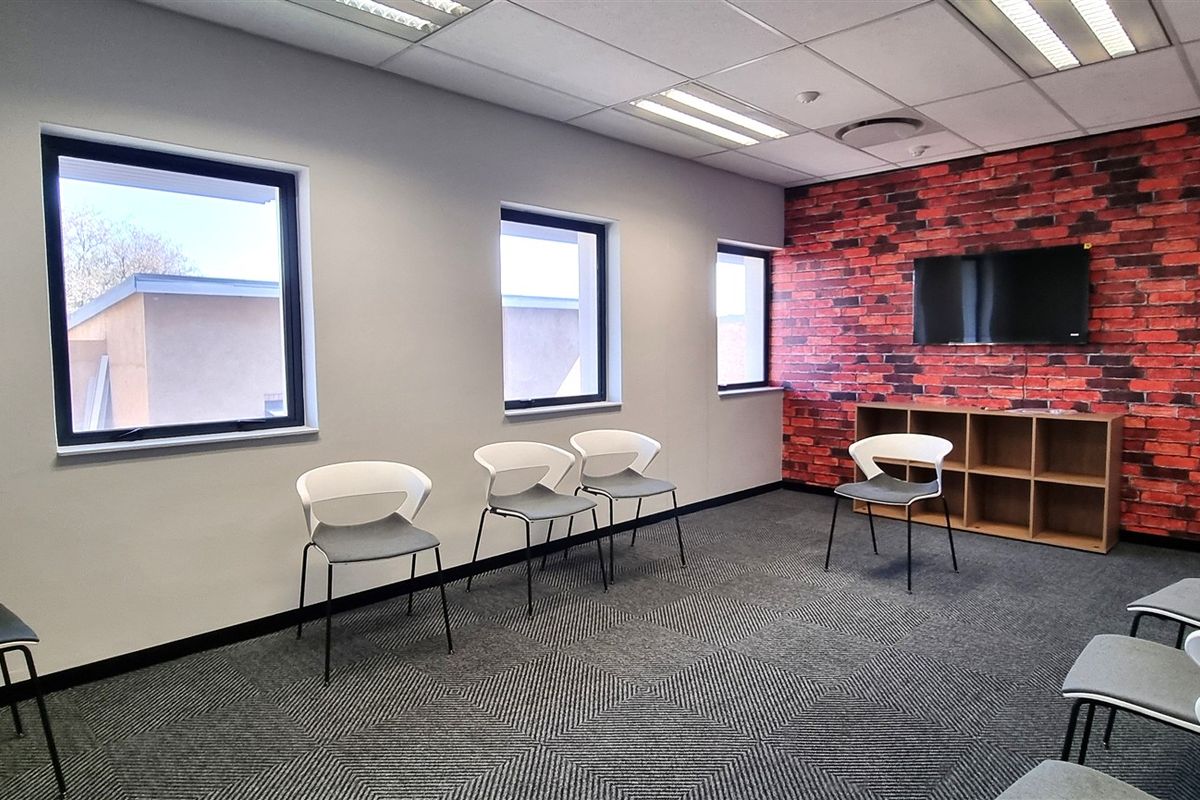A modern office space featuring carpet tiles, a brick-effect feature wall, and recessed lighting, providing a professional environment for meetings or collaborative work.