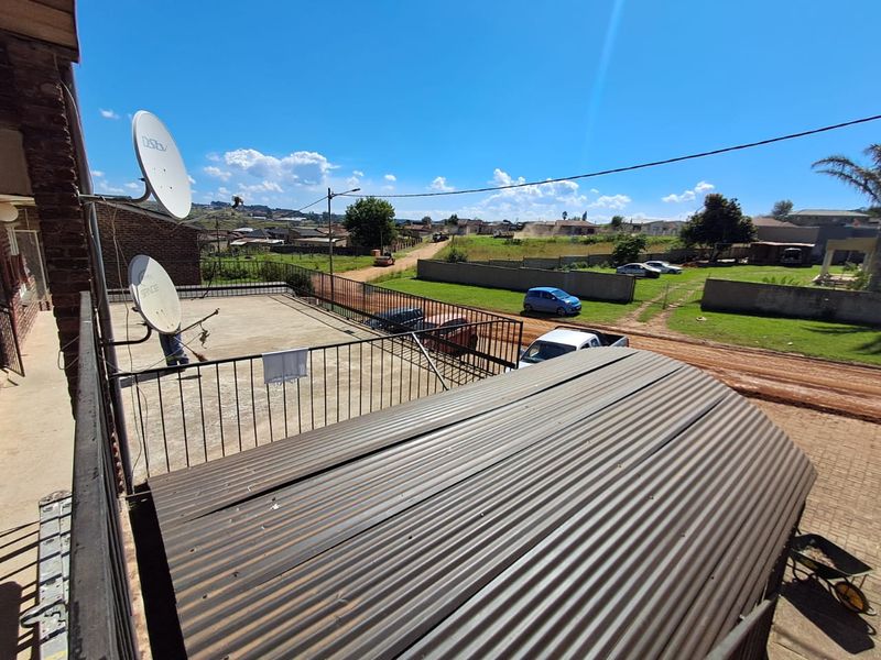 An elevated balcony area featuring a metal railing and corrugated roof, overlooking the surrounding neighborhood and street.