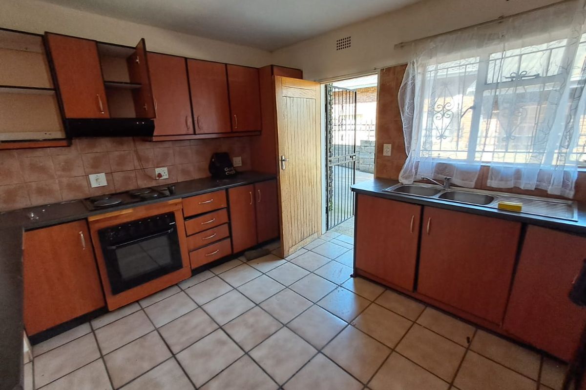 A functional kitchen featuring wooden cabinetry, built-in oven and hob, double sink, and direct access to an exterior area through a security gate.