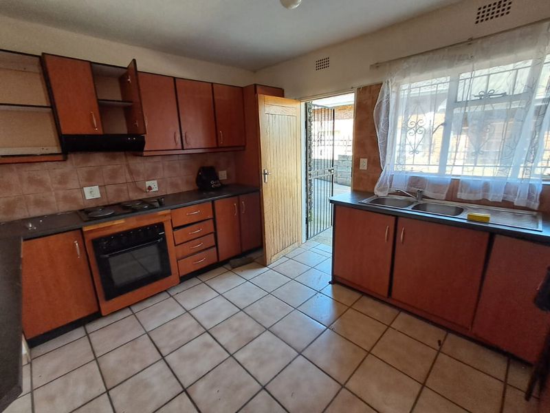 A functional kitchen featuring wooden cabinetry, built-in oven and hob, double sink, and direct access to an exterior area through a security gate.