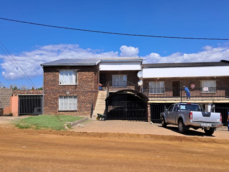 Front elevation of a multi-unit face brick apartment building featuring a paved driveway, metal security gates, and balcony access.