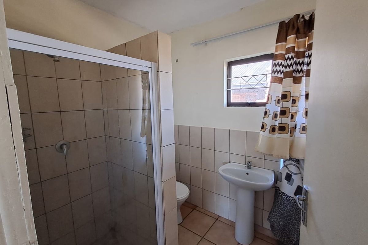A functional bathroom featuring a shower enclosure, pedestal basin, and toilet, finished with neutral wall and floor tiles.