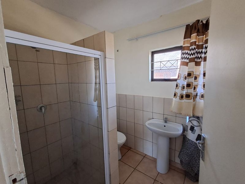 A functional bathroom featuring a shower enclosure, pedestal basin, and toilet, finished with neutral wall and floor tiles.