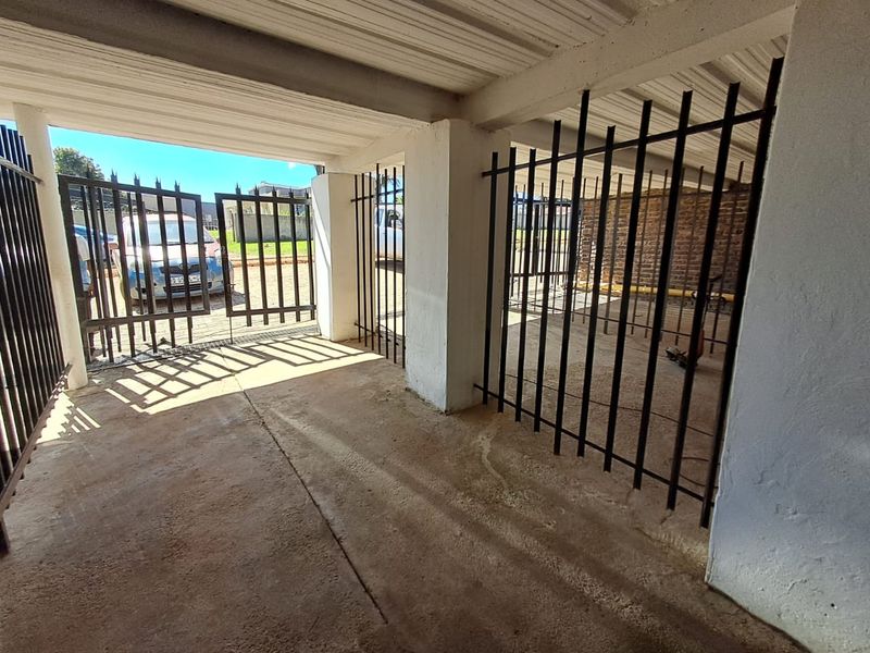 A covered parking area or garage featuring concrete flooring, exposed brickwork, and secure metal gate access.