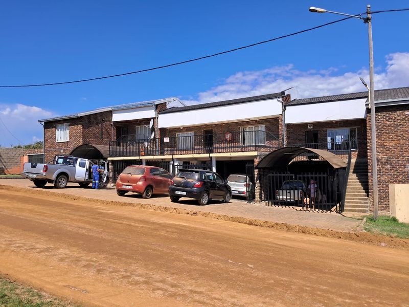 Front elevation of a multi-unit apartment complex featuring face-brick construction, external staircases, and covered parking bays.