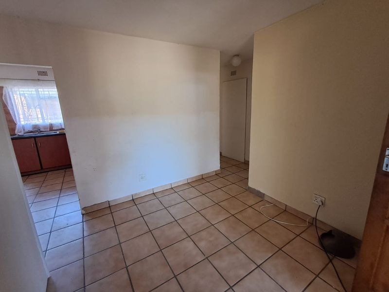 An empty living area featuring ceramic floor tiles and neutral walls, with a view into the adjacent kitchen space.
