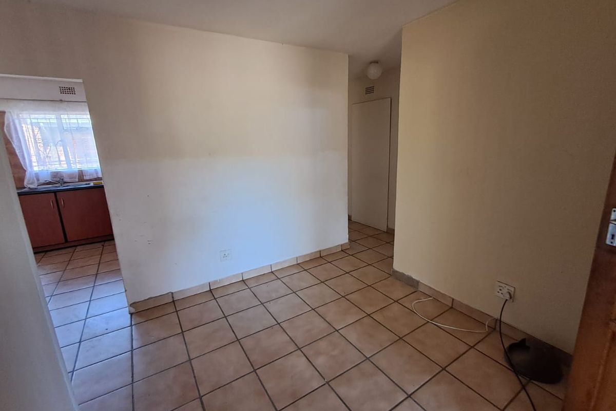 An empty living area featuring ceramic floor tiles and neutral walls, with a view into the adjacent kitchen space.
