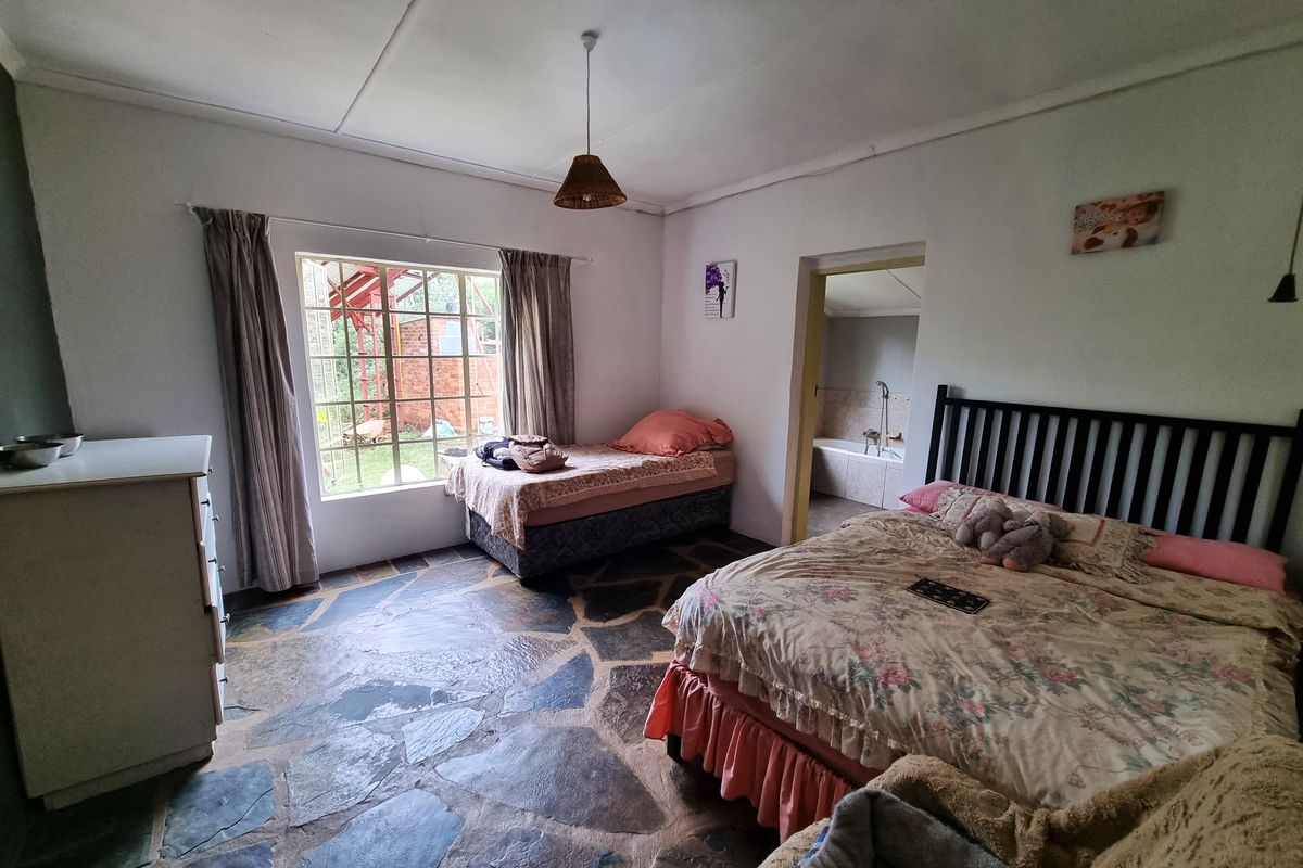 Spacious bedroom featuring unique natural stone flooring, large window providing garden views, and an adjoining bathroom access point.