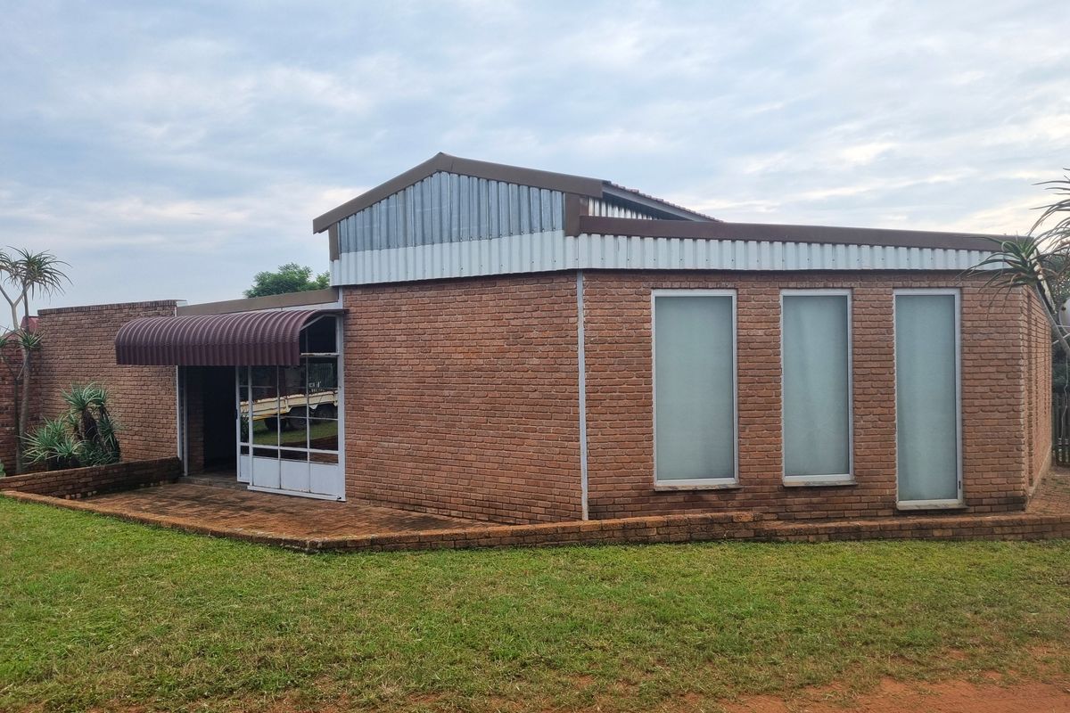 Rear view of a face brick farm building featuring a corrugated metal roof, paved patio area, and frosted glass windows.