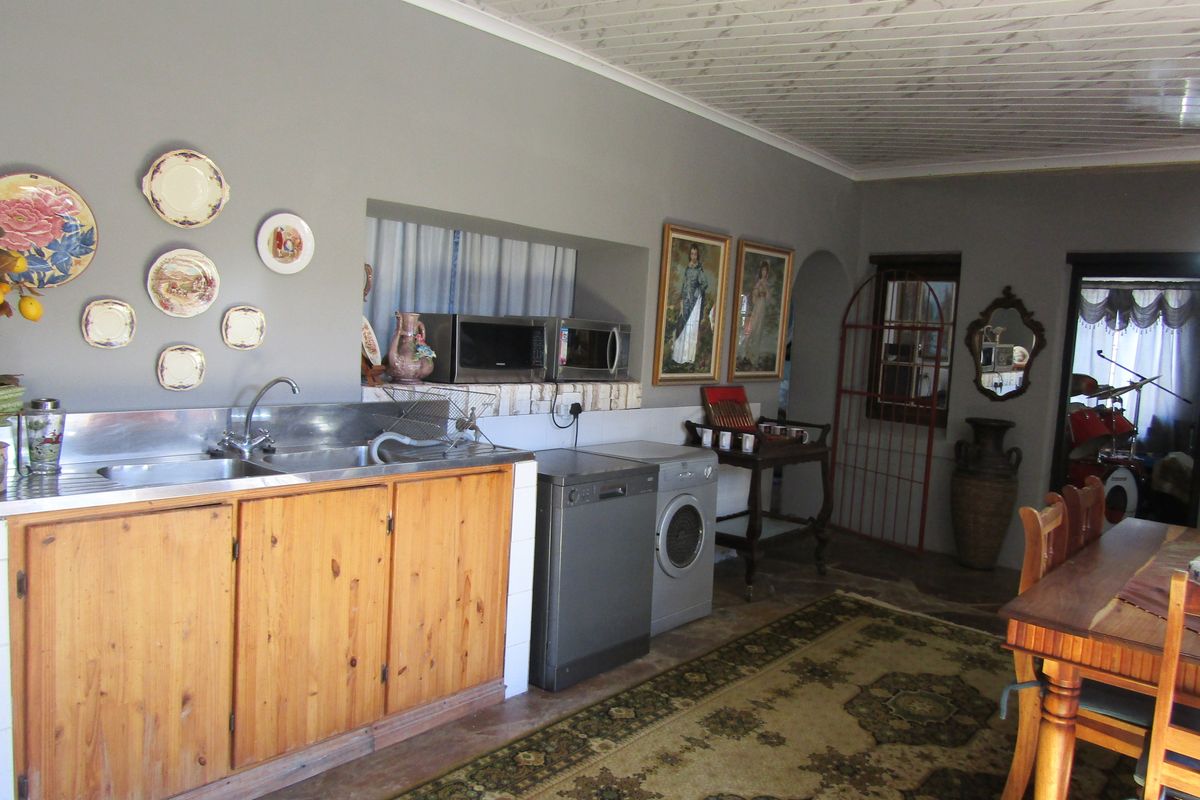 A functional kitchen area featuring wooden cabinetry, a stainless steel sink, and a tiled splashback, with an adjacent dining space.