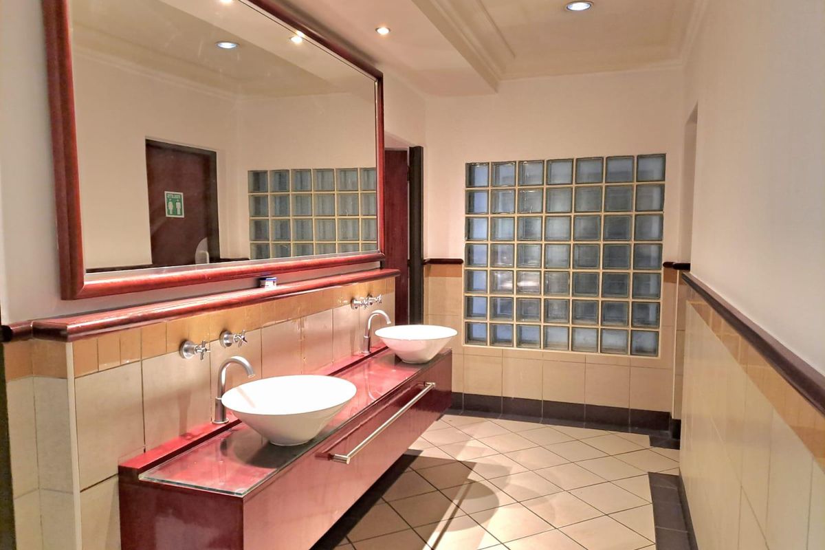 A commercial restroom featuring a dual vessel sink vanity, large wall mirror, glass block feature wall, and tiled flooring.