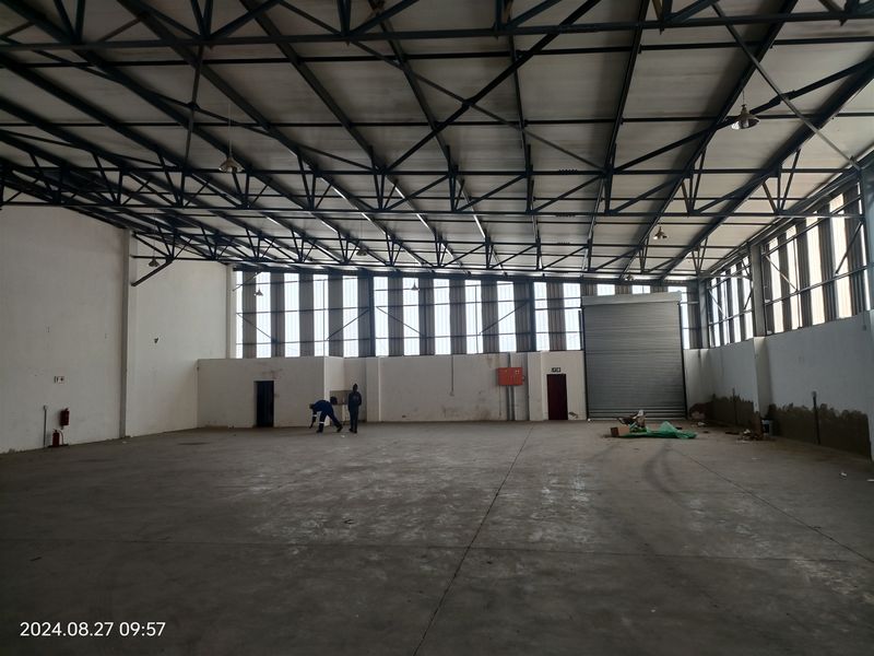 Spacious industrial warehouse featuring high ceilings with exposed steel trusses, concrete flooring, and a large roller shutter door for efficient access.