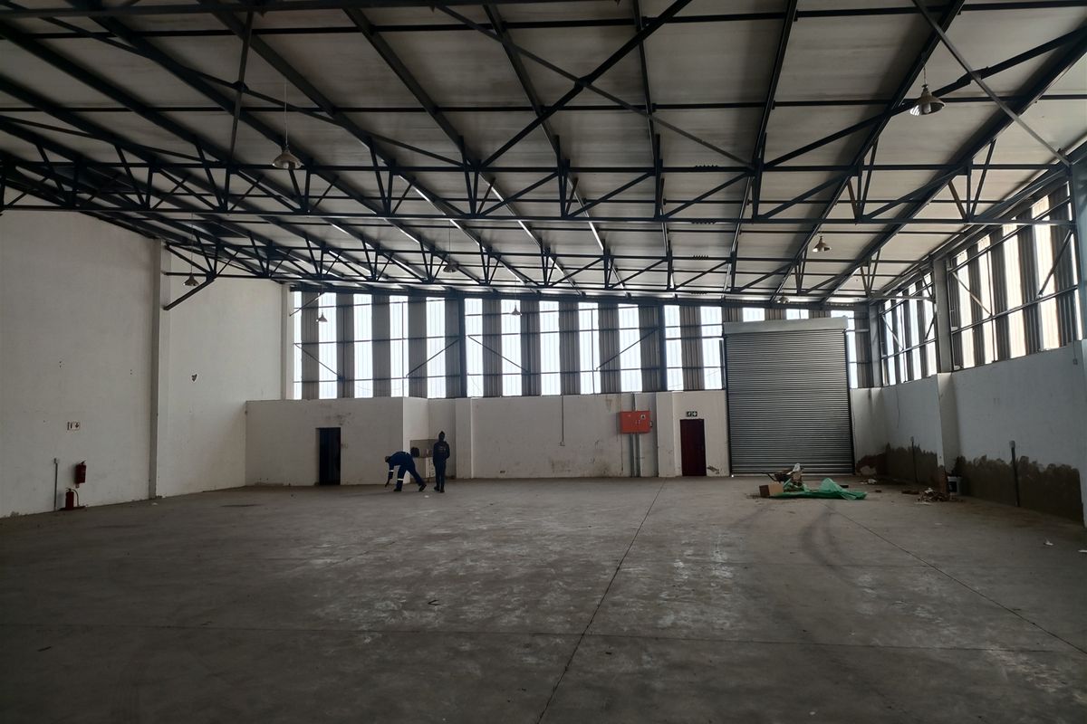 Spacious industrial warehouse featuring high ceilings with exposed steel trusses, concrete flooring, and a large roller shutter door for efficient access.