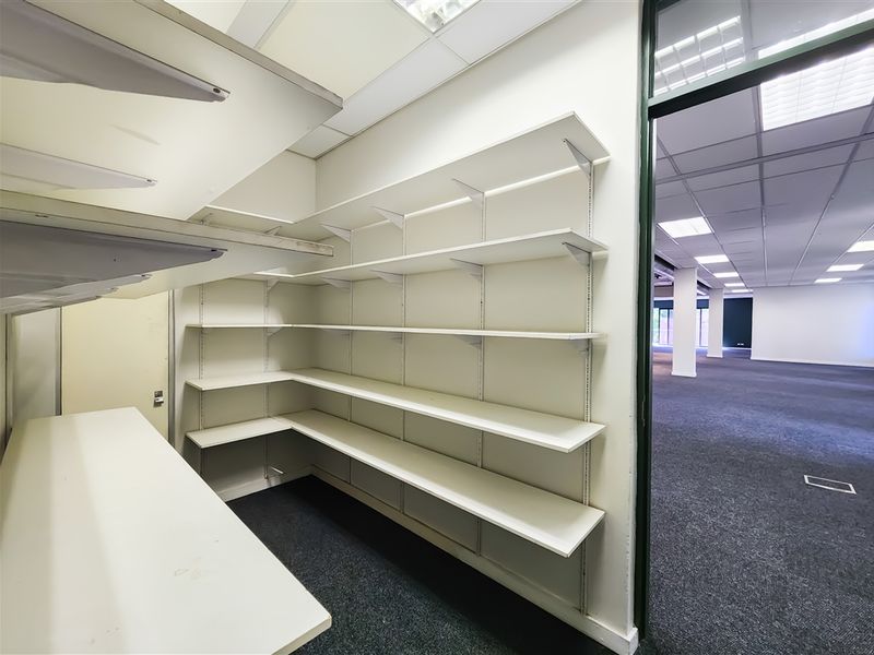 A clean, functional utility or storage room featuring extensive built-in shelving, carpeted flooring, and a suspended ceiling with recessed lighting.