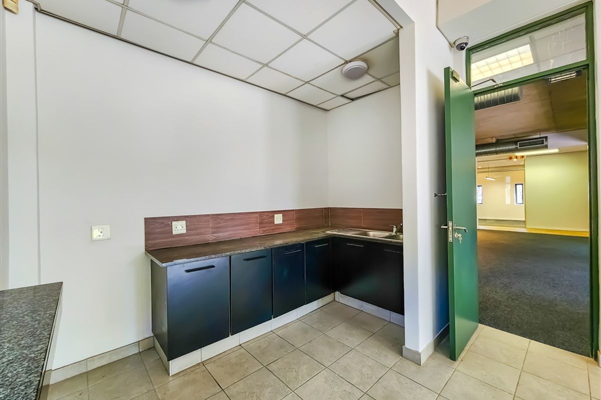 A compact office kitchenette featuring dark built-in cabinetry, a stainless steel sink, and tiled flooring, providing a functional utility space.