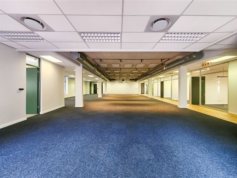 Spacious open-plan office area featuring a suspended ceiling, exposed industrial ductwork, glass partitioning, and carpeted flooring, offering a versatile professional workspace.