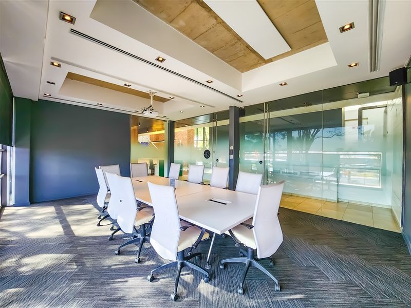 Modern professional boardroom featuring glass partitions, recessed lighting, and an exposed concrete ceiling detail, creating a bright and functional workspace.