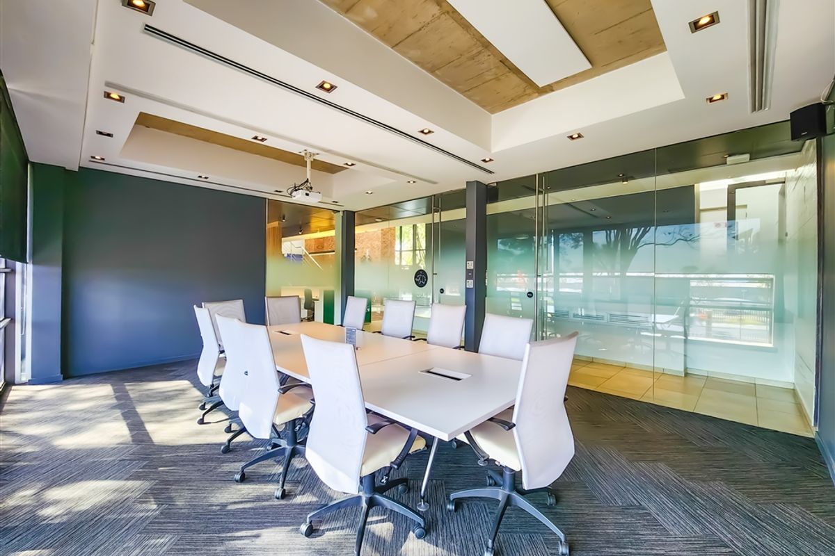 Modern professional boardroom featuring glass partitions, recessed lighting, and an exposed concrete ceiling detail, creating a bright and functional workspace.