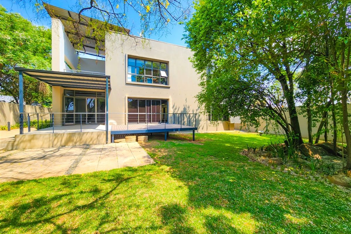 Rear view of the office building featuring a raised timber deck, paved patio area, and well-maintained garden with mature trees.