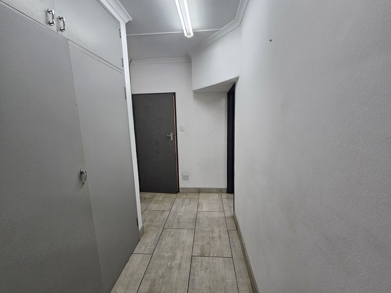 A functional office hallway featuring tiled flooring, built-in storage cupboards, and overhead fluorescent lighting.