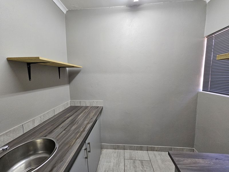 A clean and functional scullery area featuring a stainless steel sink, laminate countertops, built-in cabinetry, and tiled flooring.