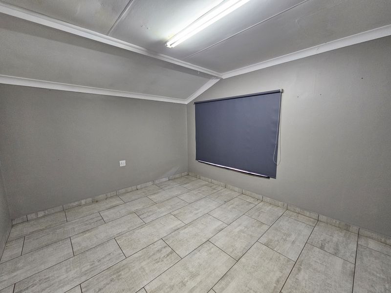 A vacant office space featuring neutral grey walls, tiled flooring, and a fitted roller blind, providing a clean and functional workspace environment.