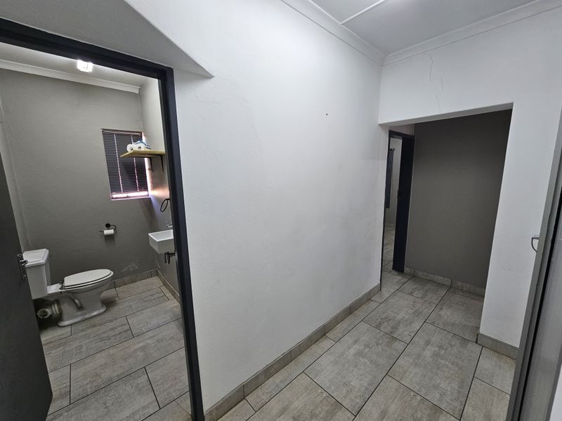 A neutral hallway area with tiled flooring, providing access to an adjacent bathroom and other office spaces.