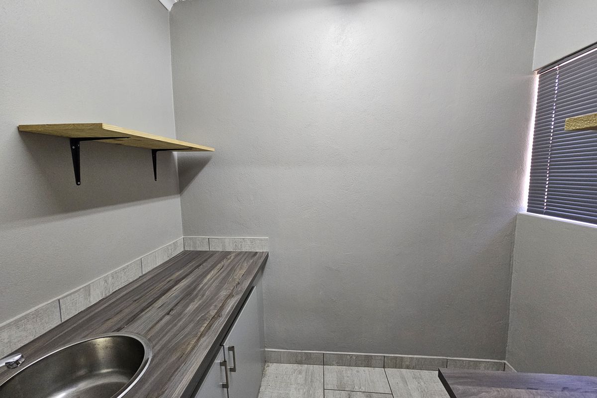 A clean and functional scullery area featuring a stainless steel sink, laminate countertops, built-in cabinetry, and tiled flooring.