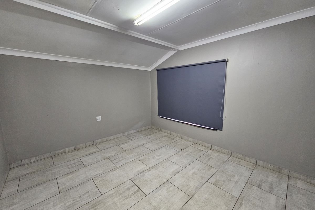 A vacant office space featuring neutral grey walls, tiled flooring, and a fitted roller blind, providing a clean and functional workspace environment.