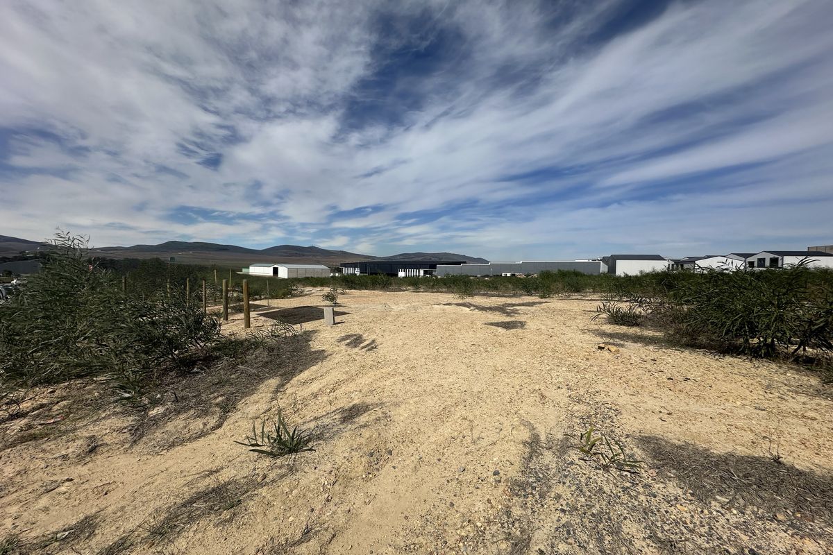 An expansive, undeveloped industrial plot featuring natural terrain and distant views of existing industrial structures under a clear sky.