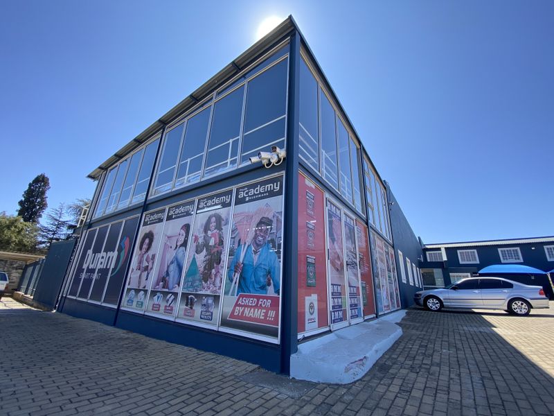 A modern two-story commercial retail building featuring extensive glass frontage, prominent branding signage, and a paved exterior parking area.