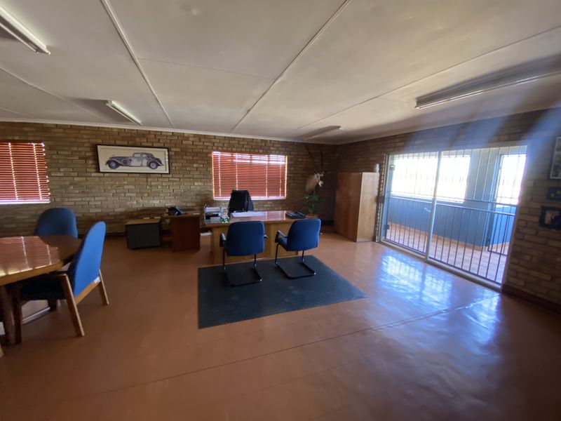 Spacious office area featuring exposed brick walls, painted concrete flooring, and large sliding glass doors leading to an outdoor balcony.