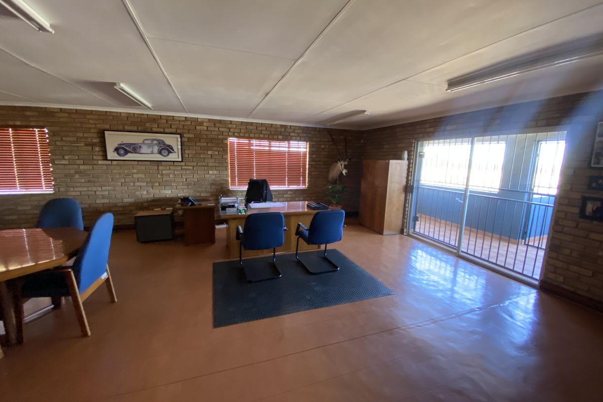 Spacious office area featuring exposed brick walls, painted concrete flooring, and large sliding glass doors leading to an outdoor balcony.