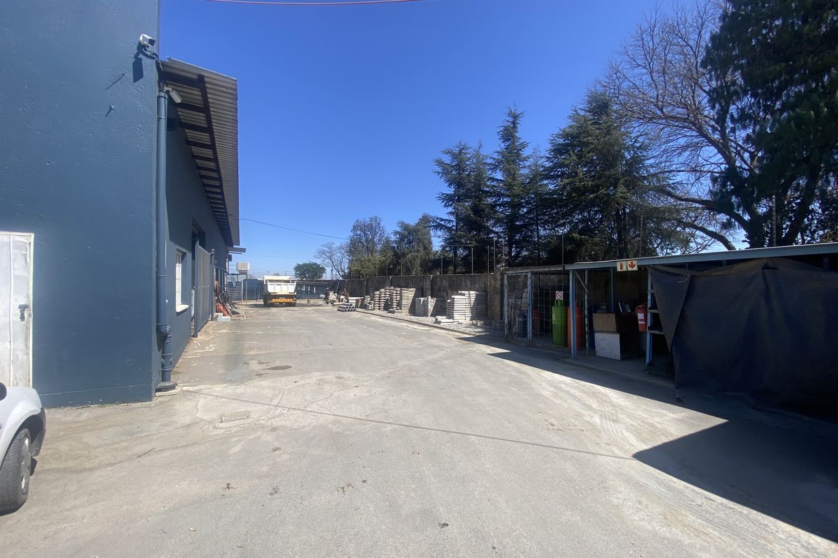 Rear exterior area of the retail property featuring an asphalt driveway, covered storage space, and perimeter walling.