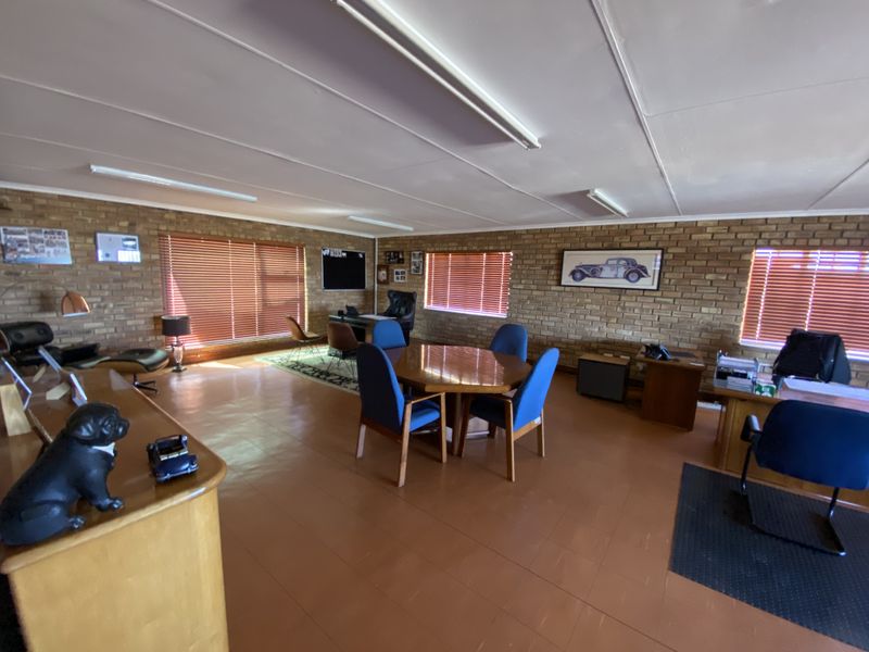 Spacious office area featuring exposed brick walls, large windows with venetian blinds, and functional overhead fluorescent lighting.