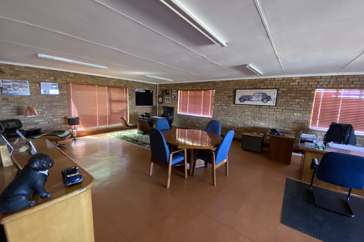 Spacious office area featuring exposed brick walls, large windows with venetian blinds, and functional overhead fluorescent lighting.