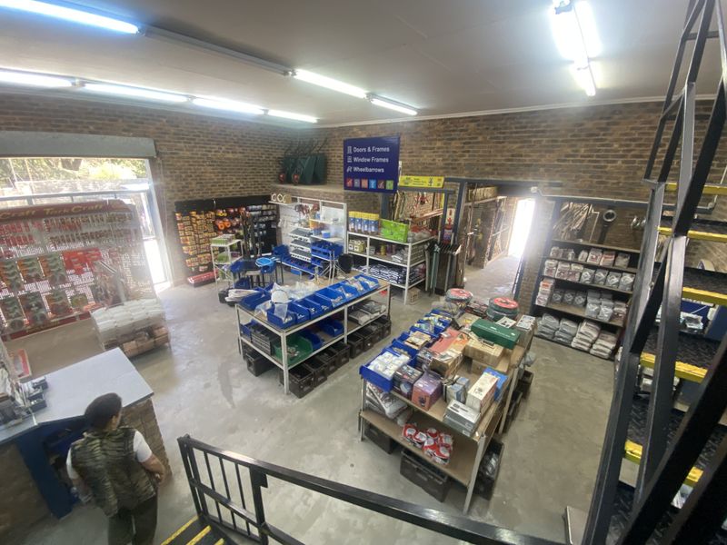 A retail hardware store interior featuring exposed brick walls, concrete flooring, and industrial fluorescent lighting with various shelving units for merchandise.